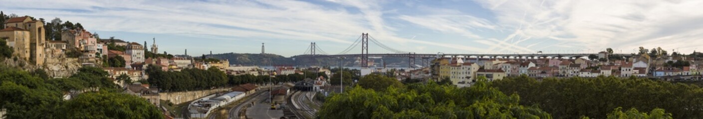 panoramic view of Lisbon with the 25 de Abril Bridge, the Christ the King statue, railroad, numerous variegated houses and evening skyscape