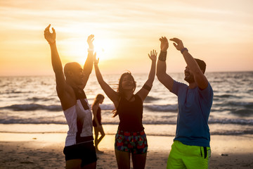 Group of people doing exercises at the beach. They are jumping with hands up in the air.