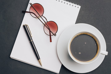 glasses and a pen on a notepad, a cup of coffee in a saucer