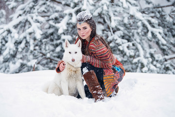 Native indian woman with traditional makeup and hairstyle in snowy winter. Beautiful girl in ethnic dress hugging an eskimo dog. - obrazy, fototapety, plakaty