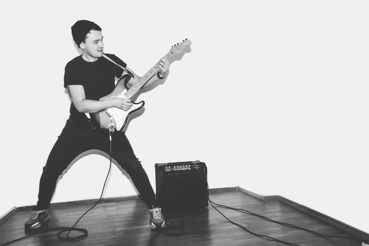 Awesome crazy fashion young musician rock guitar player jumps with passion in studio. Stylish rocky emotional man. Black and white toned.