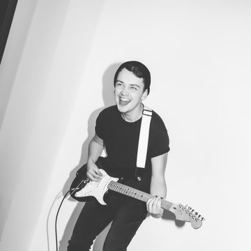 Awesome crazy fashion young musician rock guitar player jumps with passion in studio. Stylish rocky emotional man. Black and white toned.