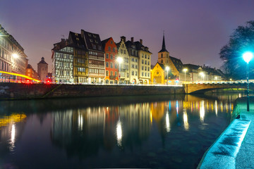 Fototapeta na wymiar Picturesque quay and church of Saint Nicolas with mirror reflections in the river Ile during evening blue hour, Strasbourg, Alsace, France