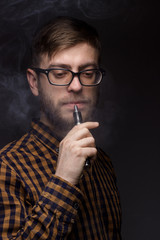 man with a beard wearing glasses on black background smoke Vape. large portrait of . electronic...