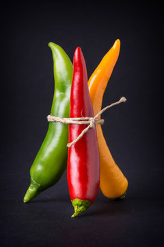 Bunte gefesselte Chilis vor schwarzem Hintergrund