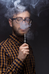 man with a beard wearing glasses on black background smoke Vape. large portrait of . electronic...