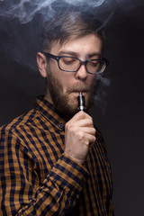 man with a beard wearing glasses on black background smoke Vape. large portrait of . electronic cigarette. E- for vaping. Popular devices  the year - modern device. Stop smoking,