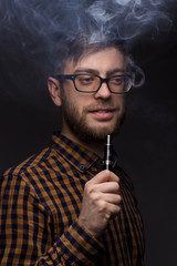 man with a beard wearing glasses on black background smoke Vape. large portrait of . electronic...