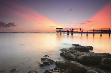 Obraz premium Beautiful sunset over wooden jetty with silhoutte of man fishing
