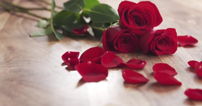 three red roses with petals and the girl writes mothers day on a paper card on old wood background, 4k prores footage