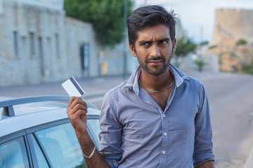 Indian young man holding showing  credit card standing next to his car outdoor background. Paying...