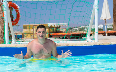 Handsome man standing at the gate in pool playing water polo