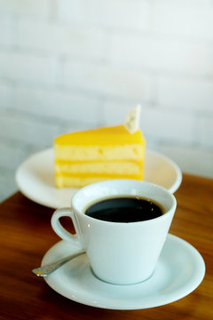 Hot black coffee and Orange cake on wooden table and white brick wall