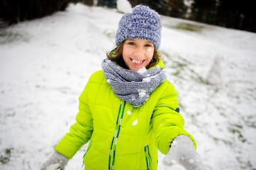 Boy of school age in bright winter overalls plays with someone in snowballs.