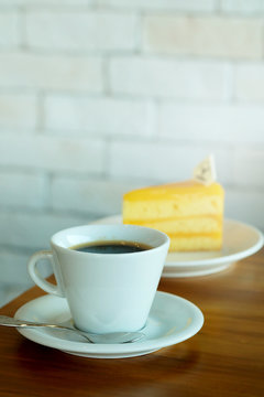 Hot black coffee and Orange cake on wooden table and white brick wall