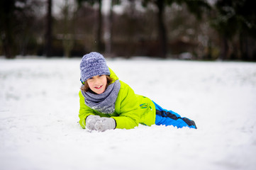 Fototapeta na wymiar The boy of school age in bright winter overalls lies on snow.
