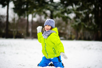 The boy of school age plays snowballs in the winter park.