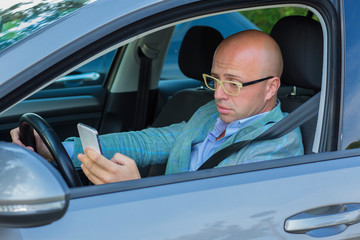 Man sitting in car with mobile phone in hand texting while driving.