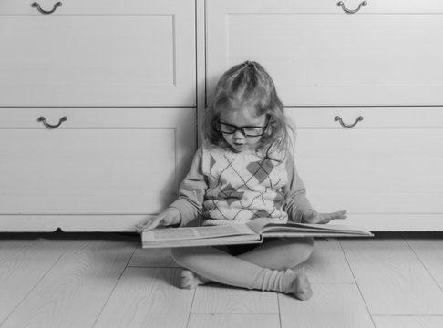 black and white, baby girl in glasses with book.