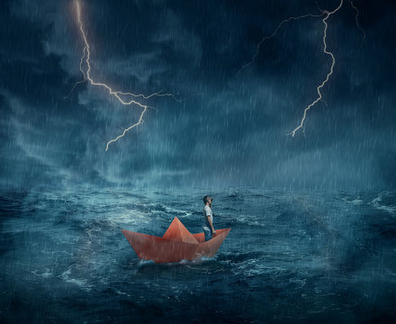 Young boy in a orange paper boat sail lost in the ocean, in a stormy night with lightnings in the sky. Adventure and journey concept.