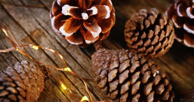 Pine cones with christmas lights on wooden plank