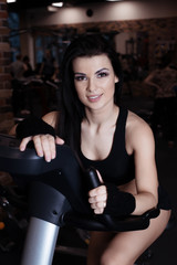 Fototapeta na wymiar Muscular young woman wearing sportswear training on exercise bikes in gym. Intense cardio workout.