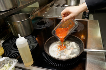 Chef is adding tomato sauce to seafood stew
