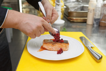 Chef is topping fried salmon steak with berry sauce