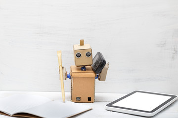 The robot holds a pen and the phone is near  laptop. Work