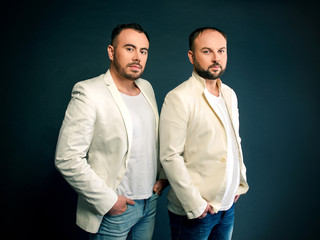 Portrait of two men in white suits on dark background