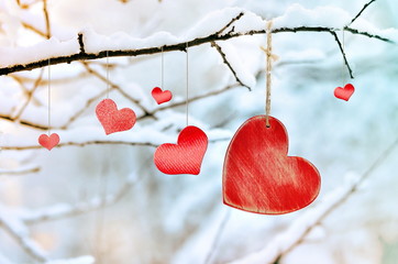 Wooden red heart on snowy tree branch in winter.