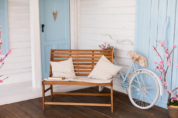 Veranda country house, bench and bicycle. yard with cherry blossoms near the house. White Bicycle With Beautiful Flower Basket on vintage background in spring season