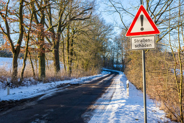 Strassenschäden - ein Hinweisschild steht im Winter an einer schmalen Landstrasse in Brandenburg (...