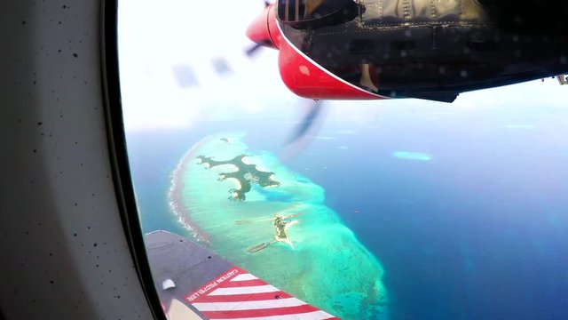 Engine of an otter twing water plane in action while flying above the maldives, showing amazing tiny colorful islands and unique turquoise color of the indian ocean. 