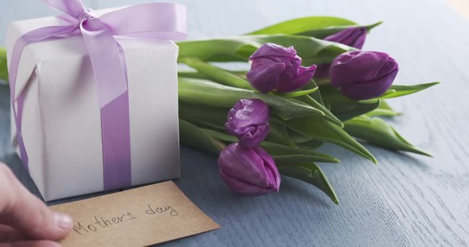 man put mothers day greeting card on blue table with purple tulips and gift box on it, 4k 60fps prores footage