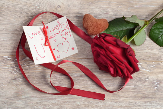 Valentine's day concept with toy heart, hand write love message and red rose on wooden background
