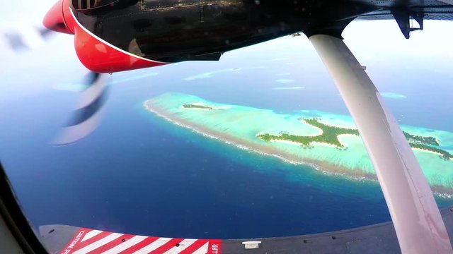Engine of an otter twing water plane in action while flying above the maldives, showing amazing tiny colorful islands and unique turquoise color of the indian ocean. 