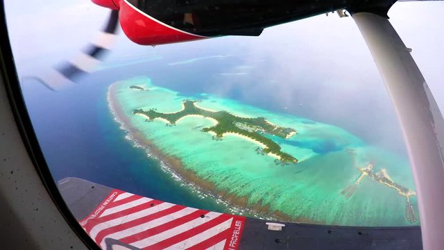 Engine of an otter twing water plane in action while flying above the maldives, showing amazing tiny colorful islands and unique turquoise color of the indian ocean. 