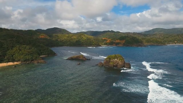 The coast of the tropical island with the mountains and the rainforest on a background of ocean with big waves.Aerial view: sea and the tropical island with rocks, beach and waves. Seascape: sky
