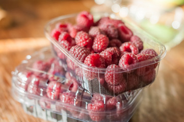 Fresh raspberry in plastic boxes from supermarket on kitchen table, kitchen interior in the background