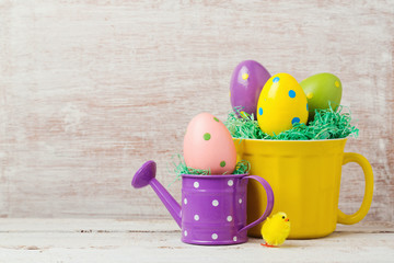 Easter holiday concept with painted eggs decoration, cup and watering can over rustic background