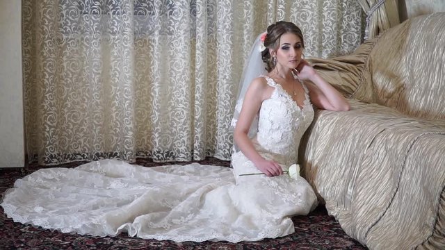 Thoughtful bride with sad eyes is sitting beside the couch