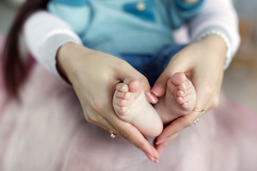 My mother's delicate hand,nails painted pink varnish,with folded hands in the shape of a heart,keeps the feet of his newborn son,the child sitting in the mother on her knees,dressed in a blue shirt