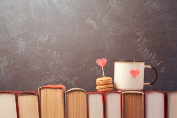 Valentines day concept with retro tea cup and macarons dessert on books over blackboard background
