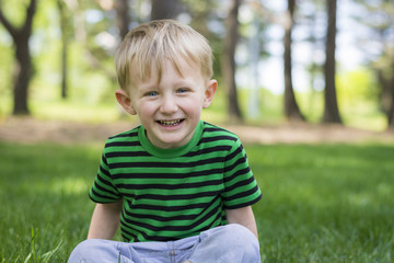 Happy young boy sitting in the grass at the park