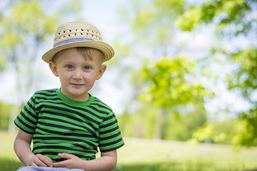 Young boy sitting in the grass at the park wearing a fedora