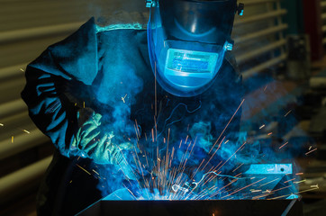 Welder welds metal parts in a protective suit