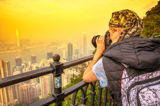 Traveler asian concept. Close up of young photographer with professional camera from back, photographing the Victoria Harbour from Victoria Peak, the highest mountain in Hong Kong. Shot at sunset.