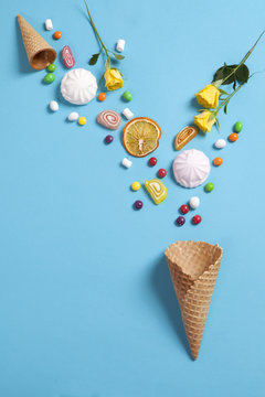 Marshmallows, candy, jelly beans, sweets and dry mugs oranges falling in wafer cone on blue background