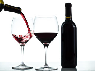 Bottle and glasses of red wine on a white background. Wine poured in one glass from a bottle.